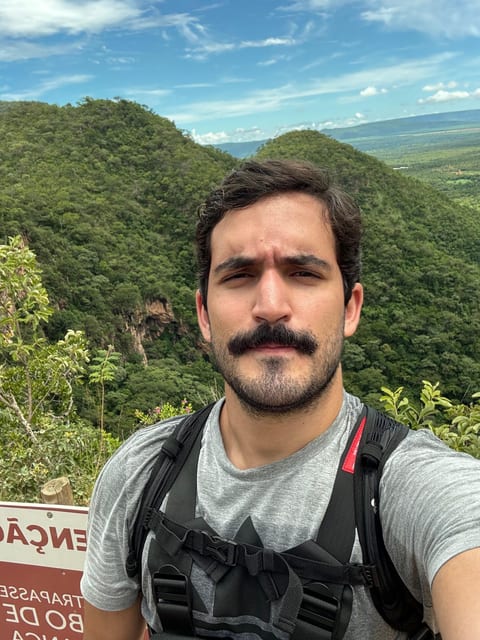 Pedro Batista on a hiking trail, with forested hills behind him